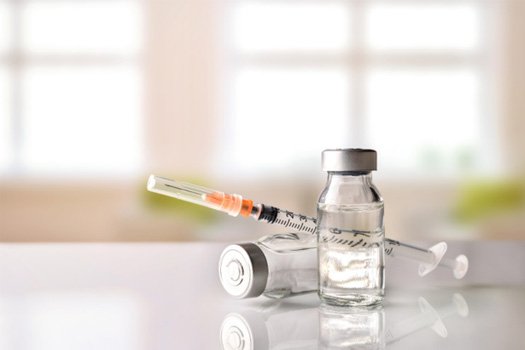 Bottles of clear liquid and injection needle on white surface