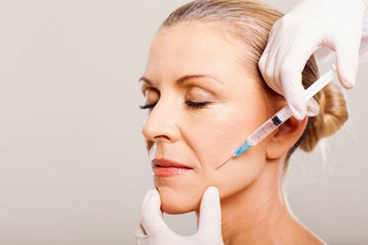 Woman with gray hair and eyes closed receiving facial injection