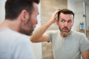 man looking in the mirror at hair loss