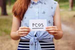 woman holding a paper with PCOS on it